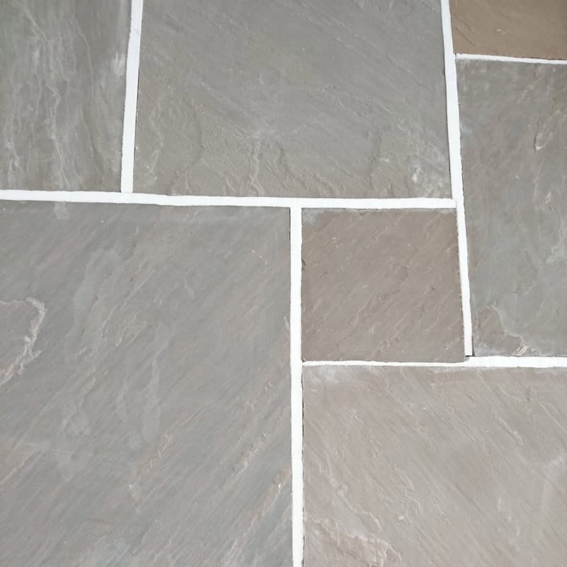Close-up image of Strata 22mm Calibrated Sandstone RAJ flooring, featuring a geometric pattern with rectangular tiles. Reminiscent of natural sandstone, these tiles vary in shades of gray with white grout and a slightly rough texture.