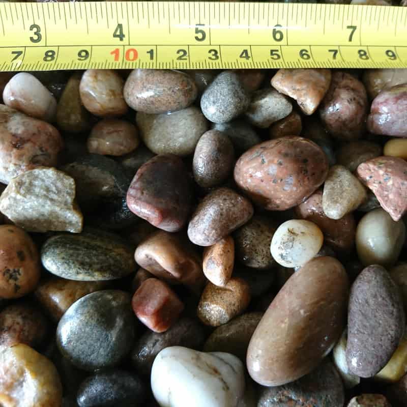 Under a measuring tape marked in centimeters, the Scottish Highland Pebbles 14-20mm - Bagged are displayed, with individual stones reaching up to approximately 10 cm.