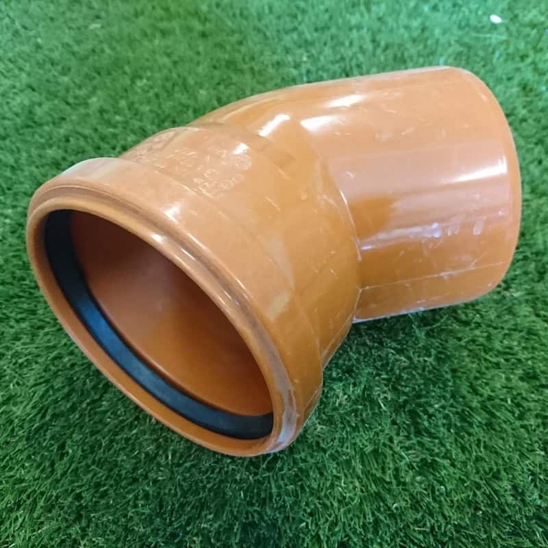 A 110mm 45° Single Socket Bend pipe, crafted from brown plastic with a rubber lining, rests on a grassy surface.