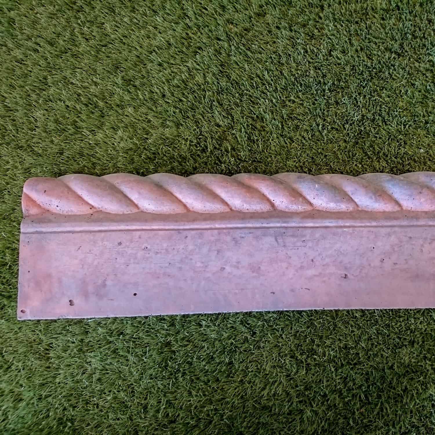 A Brett Rope Top Brindle Edging piece lies on grass, its aged-look stone molding enhances its rustic charm.
