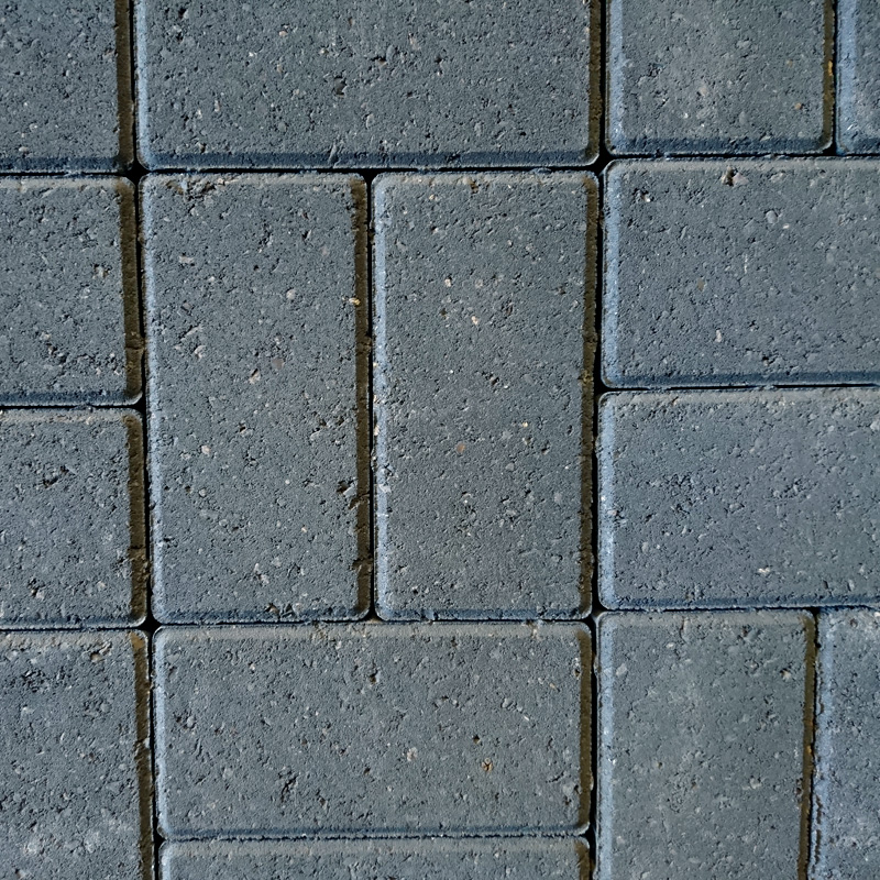 Close-up of a pavement with rectangular tiles in a grid pattern. The Breedon 50mm Drive Charcoal tiles are uniformly gray, slightly rough-textured, with thin gaps showing subtle charcoal tones typical of Breedon surfaces.