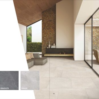 Modern indoor-outdoor space features Premier Elegance Sand 21.6m² Porcelain Pack tiles, a stone fireplace, glass wall, built-in bench, round chair, and greenery. Tile samples in sand, graphite, and grigio appear in the foreground.