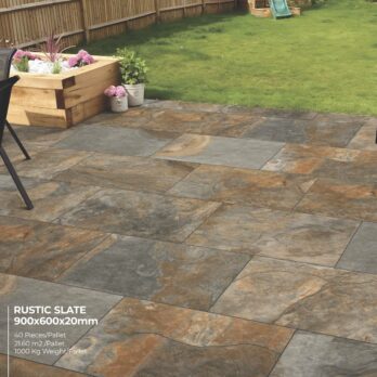 A backyard patio features Premier Avantgarde Rustic Slate 21.6m2 Porcelain tiles in gray and brown, mimicking natural Raj paving. It's bordered by a flower planter, grass lawn, and a wooden fence.