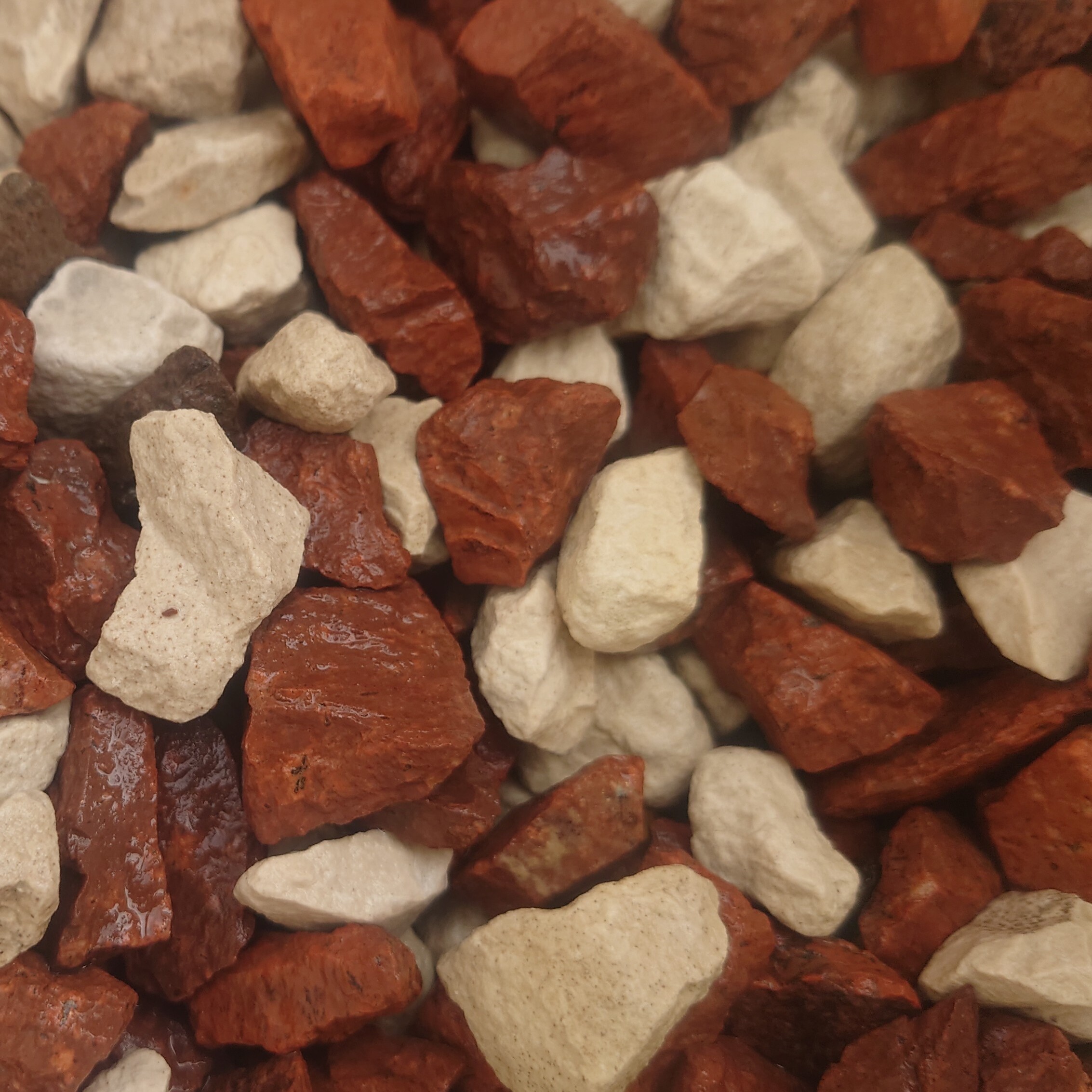 A close-up of Fire & Ice Chippings 14-20mm - Bagged reveals small, jagged white and reddish-brown stones, ideal for landscaping projects.