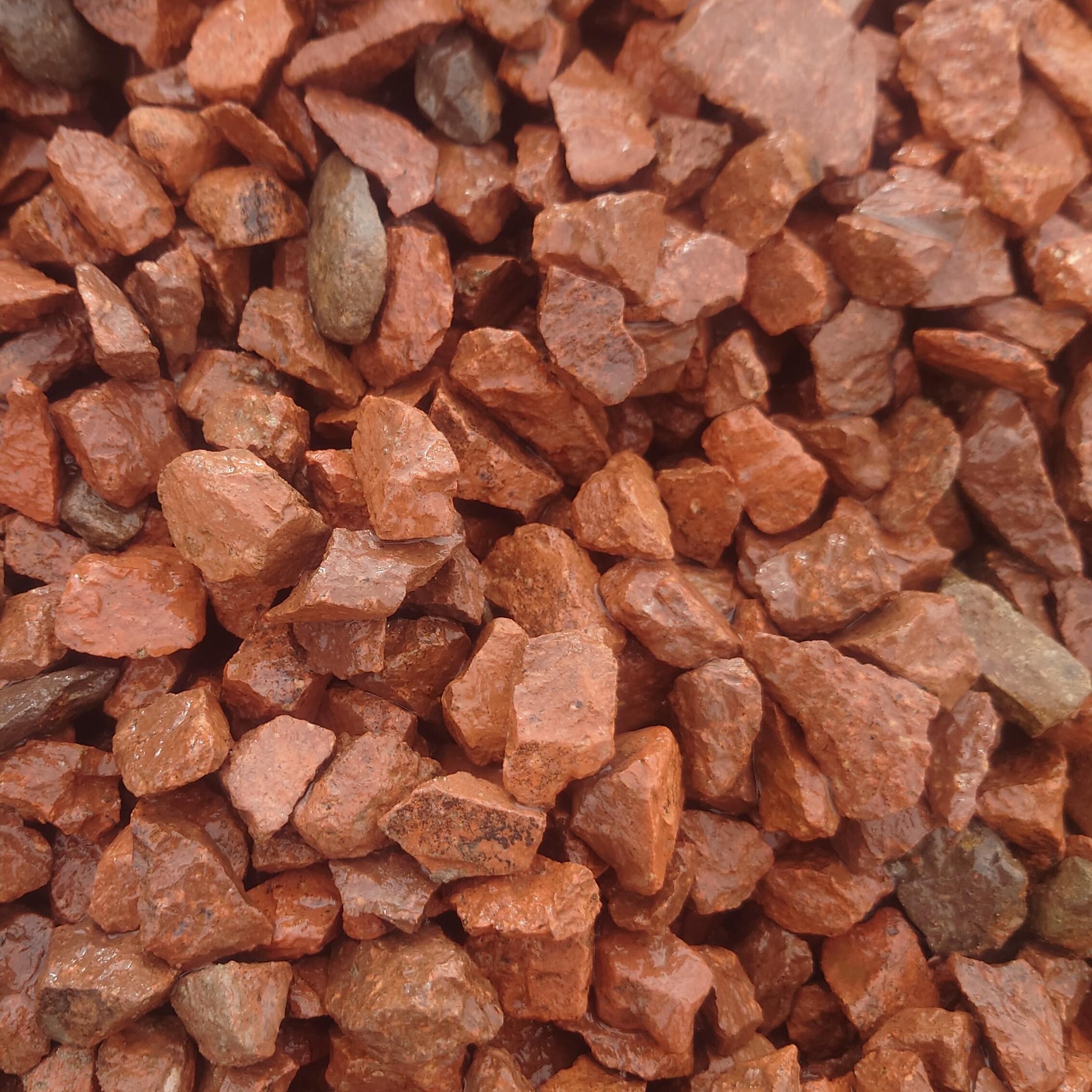 A close-up view of reddish-brown, jagged rocks highlights the varied shapes and rough textures of Red Granite 20mm - Loose or Bagged decorative stone.