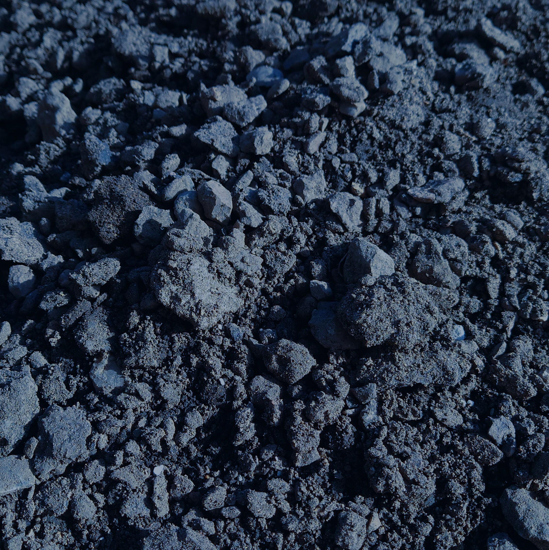 A close-up of Road Planings Graded - Loose or Bagged, showing a rough, uneven surface with dark grey soil, small stones, and scattered road planings scaplings that highlight the varied textures and clumps throughout.