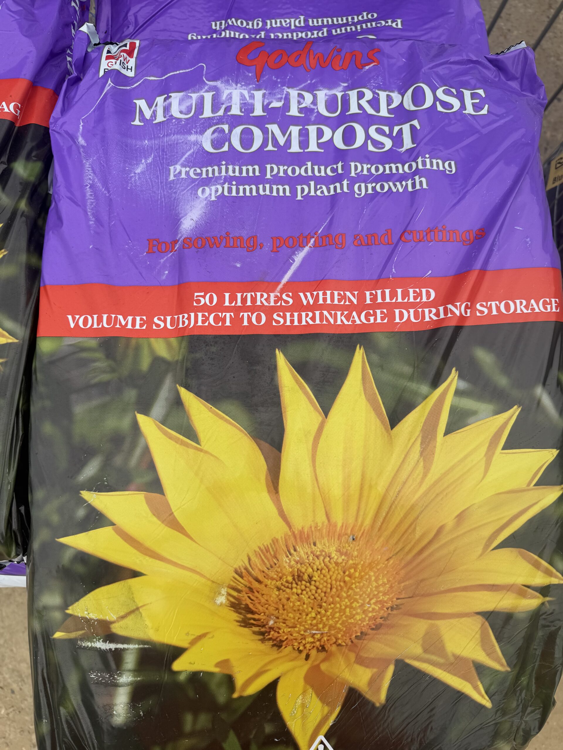 A Multi-Purpose Compost 50 litre Bag featuring a yellow flower image—suitable for sowing, potting, and cuttings. The durable packaging is designed to promote optimum plant growth and is comparable in strength to a Cement Rugby Premium 25kg waterproof bag.
